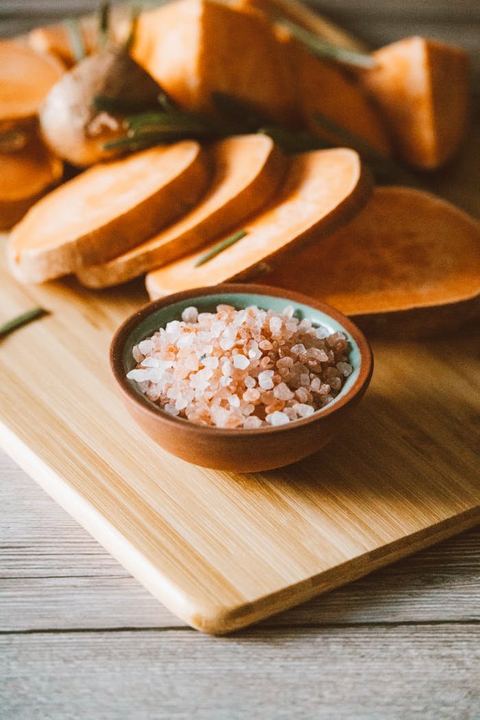 Sliced sweet potatoes on a wooden board with a bowl of Himalayan salt, perfect for culinary inspiration.